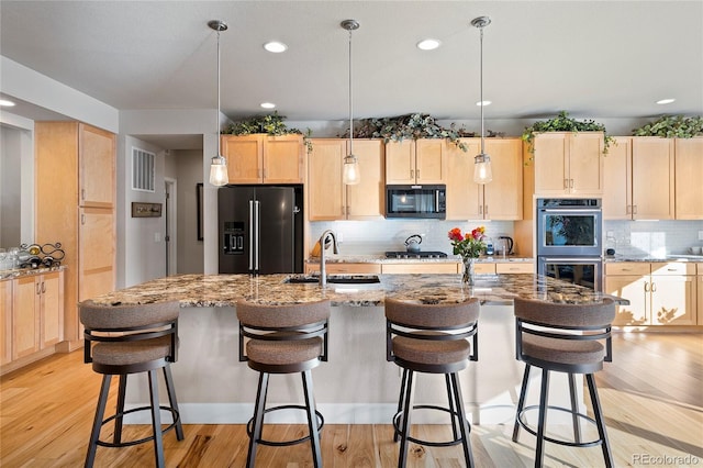 kitchen featuring light brown cabinetry, double oven, gas cooktop, high end black refrigerator, and light wood-type flooring