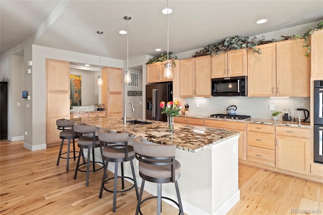 kitchen featuring a breakfast bar, backsplash, light brown cabinetry, appliances with stainless steel finishes, and light wood-type flooring