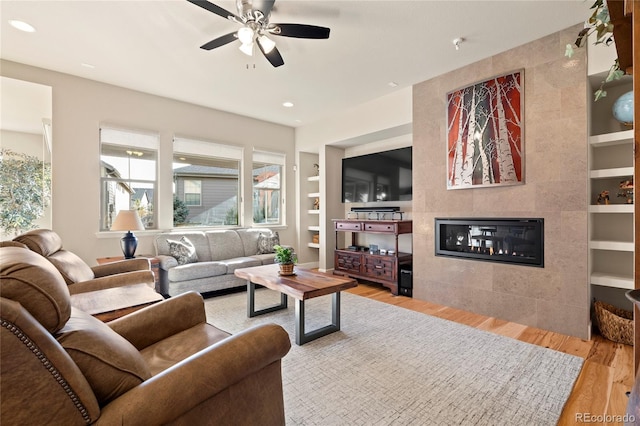 living room featuring built in shelves, recessed lighting, a fireplace, wood finished floors, and a ceiling fan