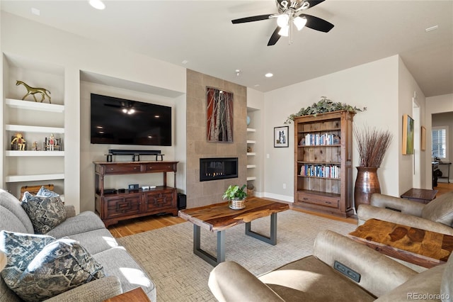 living room with ceiling fan, recessed lighting, built in features, light wood finished floors, and a tiled fireplace