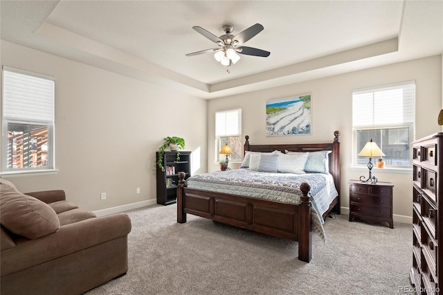 bedroom featuring light carpet, baseboards, a tray ceiling, and ceiling fan