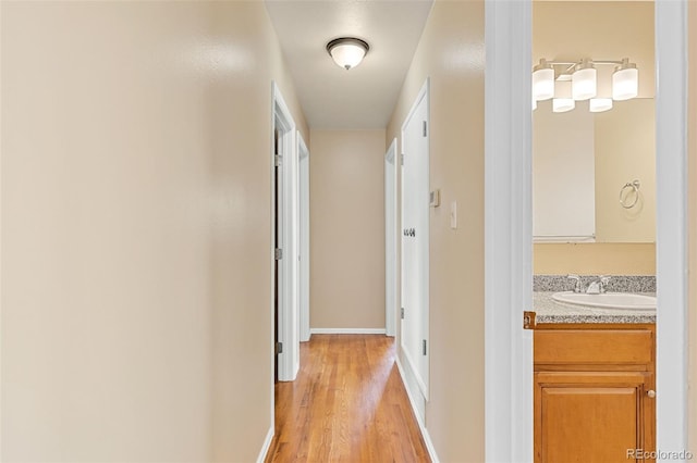 corridor featuring light wood-style flooring, baseboards, and a sink