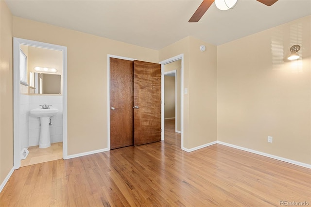 unfurnished bedroom featuring light wood-type flooring, a sink, ensuite bath, a closet, and baseboards