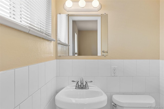 half bath with toilet, tile walls, and a sink