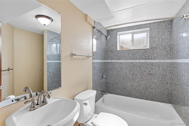 bathroom featuring a textured wall, toilet,  shower combination, and a sink