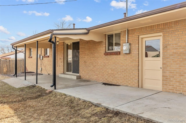 view of exterior entry featuring fence and brick siding