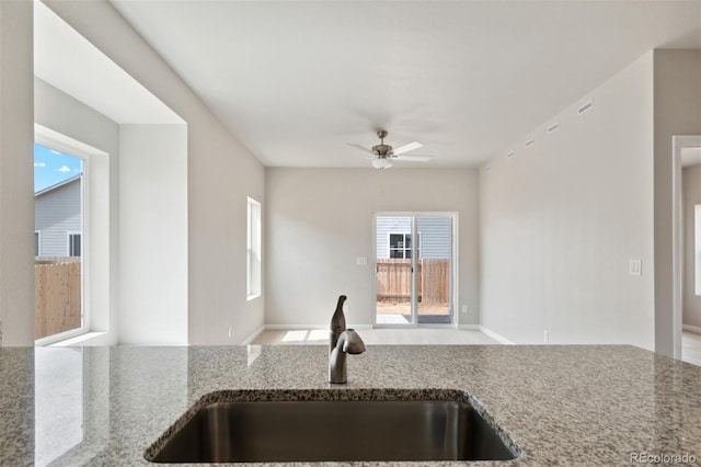 kitchen featuring ceiling fan, sink, and stone counters