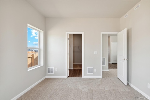 unfurnished bedroom featuring a closet, a spacious closet, and light colored carpet