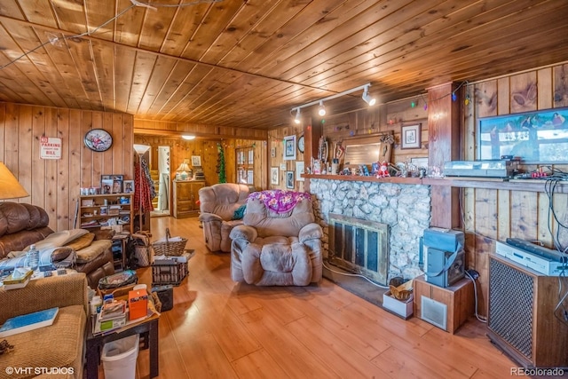 living room with a stone fireplace, wood ceiling, wooden walls, and track lighting