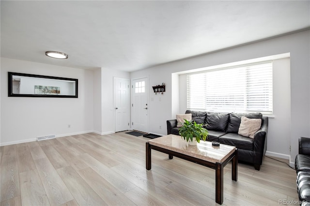 living room with light wood-type flooring, visible vents, and baseboards