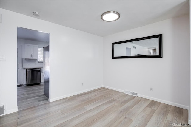 empty room with light wood-style flooring, visible vents, and baseboards