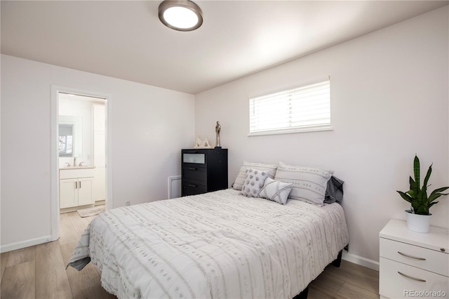 bedroom with light wood-type flooring, baseboards, a sink, and ensuite bathroom