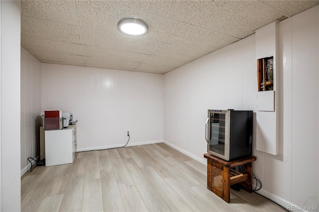 finished basement featuring beverage cooler, light wood-type flooring, a paneled ceiling, and baseboards