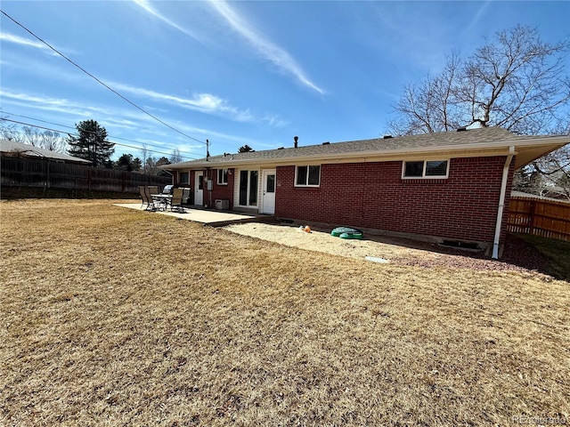 back of property featuring brick siding, a lawn, a patio area, and fence