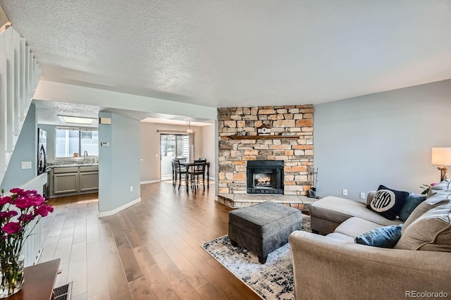 living room featuring a textured ceiling, baseboards, wood finished floors, and a stone fireplace