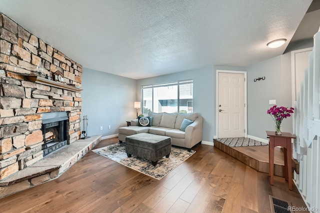 living room featuring visible vents, a stone fireplace, a textured ceiling, baseboards, and hardwood / wood-style flooring