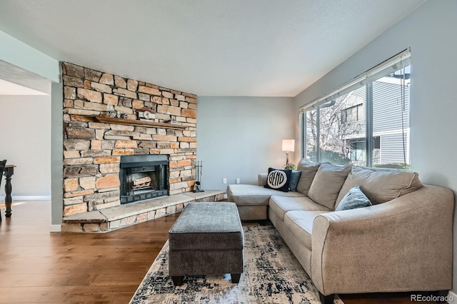 living area with baseboards, wood finished floors, and a stone fireplace