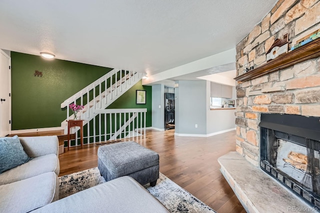 living area with stairs, a stone fireplace, baseboards, and wood finished floors