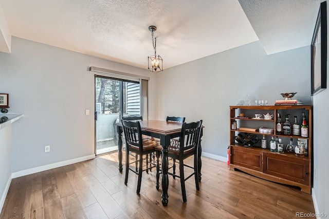 dining area featuring an inviting chandelier, a textured ceiling, baseboards, and wood finished floors