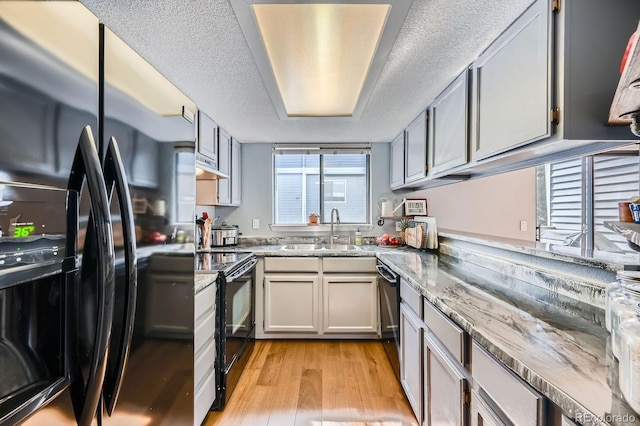 kitchen with light stone counters, light wood-style floors, a sink, a textured ceiling, and black appliances