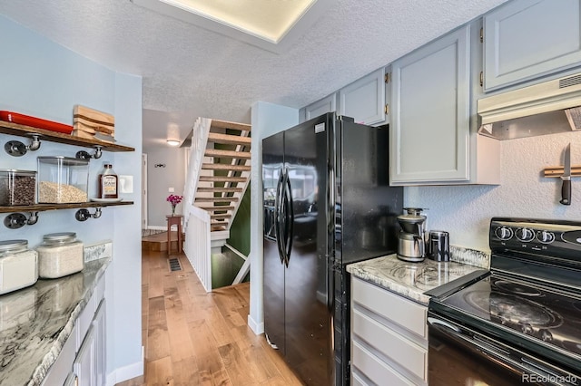 kitchen featuring light stone counters, light wood-style floors, a textured ceiling, under cabinet range hood, and black appliances