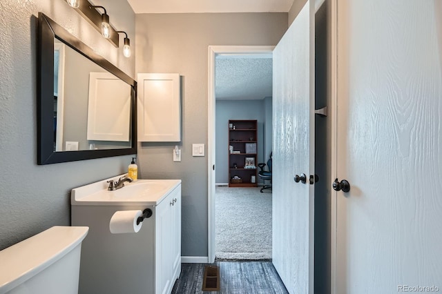 bathroom with toilet, a textured ceiling, vanity, and baseboards