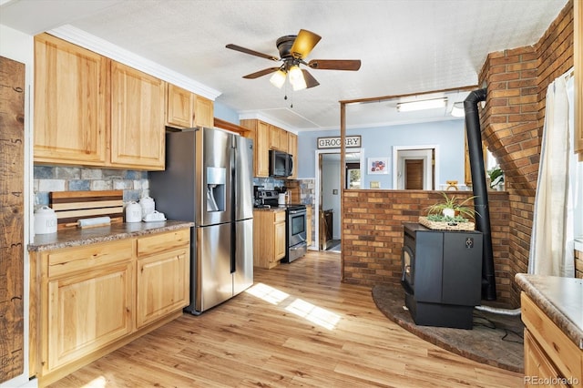 kitchen with backsplash, crown molding, light hardwood / wood-style flooring, a wood stove, and stainless steel appliances