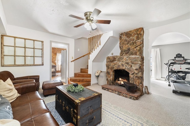 carpeted living room featuring ceiling fan, a textured ceiling, and a stone fireplace