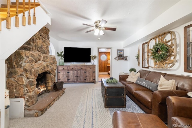 living room with ceiling fan, a textured ceiling, and a stone fireplace