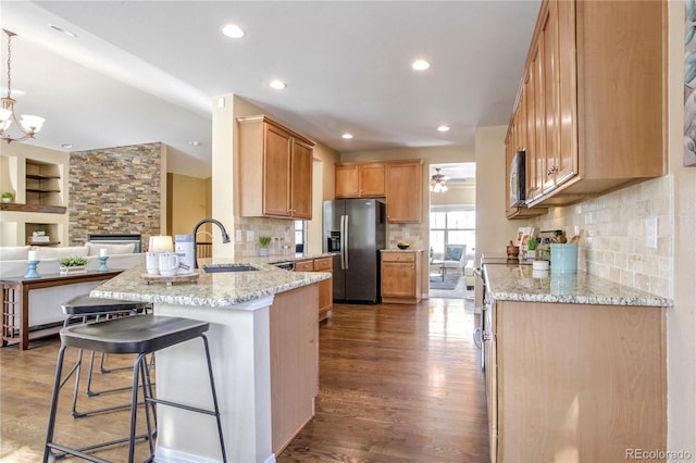 kitchen with hardwood / wood-style floors, appliances with stainless steel finishes, sink, kitchen peninsula, and light stone counters