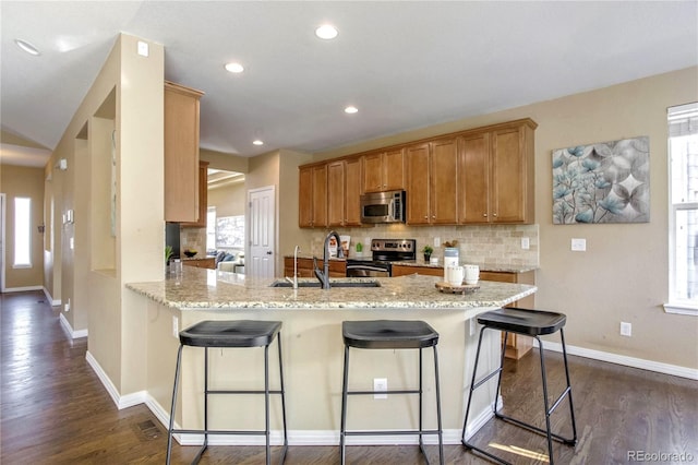 kitchen with kitchen peninsula, appliances with stainless steel finishes, sink, light stone countertops, and a breakfast bar area