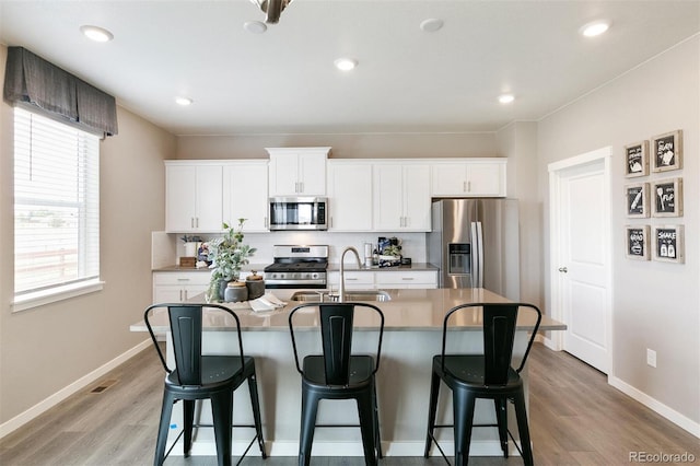 kitchen featuring light wood-type flooring, stainless steel appliances, sink, a center island with sink, and white cabinetry