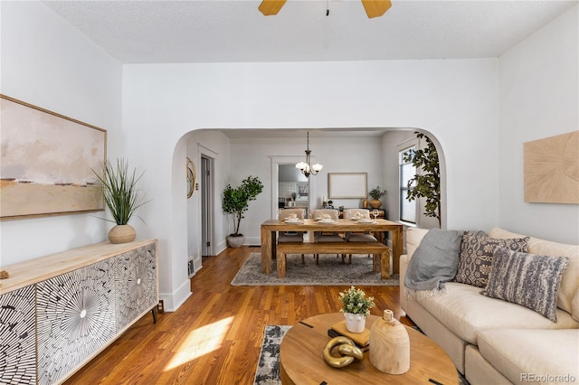 living room featuring ceiling fan with notable chandelier, hardwood / wood-style floors, and a textured ceiling