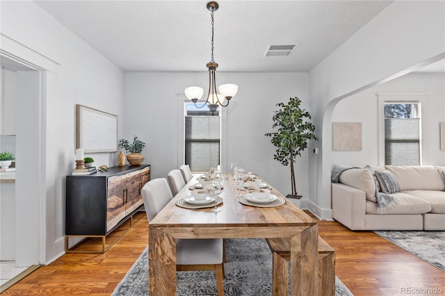 dining area with wood-type flooring, a wealth of natural light, a textured ceiling, and an inviting chandelier