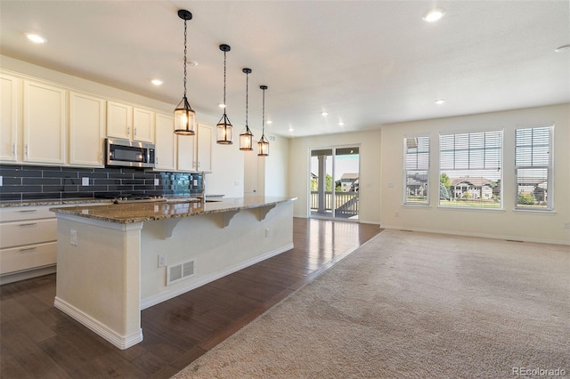 kitchen with a center island with sink, white cabinets, dark stone countertops, and dark hardwood / wood-style floors