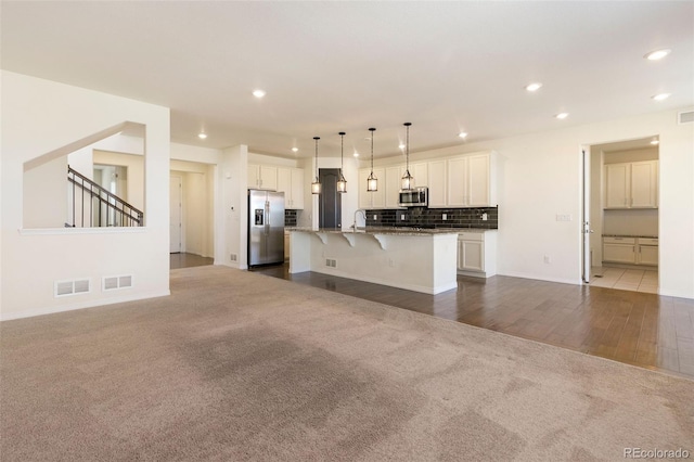 kitchen with a kitchen breakfast bar, an island with sink, wood-type flooring, white cabinets, and stainless steel appliances