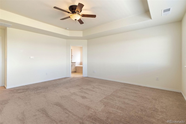 empty room with light colored carpet, a raised ceiling, and ceiling fan