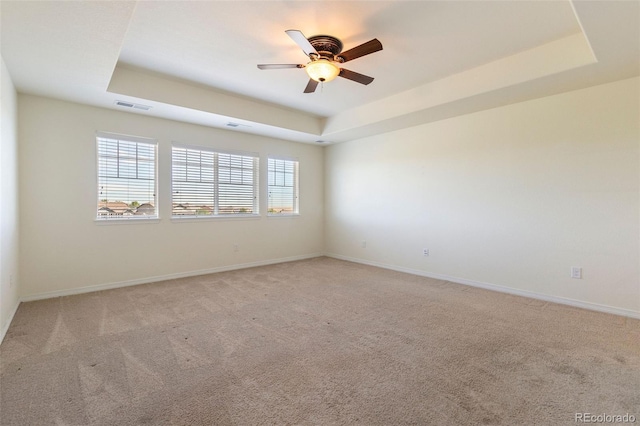 unfurnished room featuring ceiling fan, light carpet, and a tray ceiling