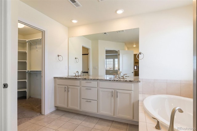 bathroom featuring tile patterned flooring, vanity, and tiled bath