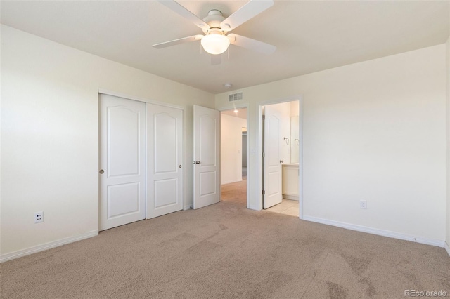 unfurnished bedroom with a closet, ceiling fan, light colored carpet, and ensuite bathroom