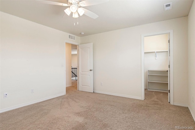 unfurnished bedroom featuring a walk in closet, a closet, ceiling fan, and light colored carpet