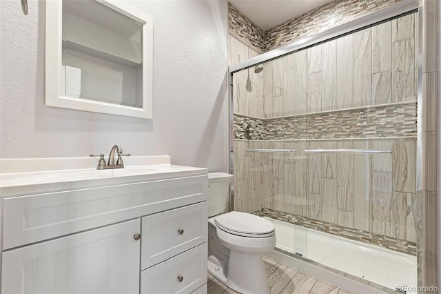 bathroom with a shower with shower door, toilet, and vanity