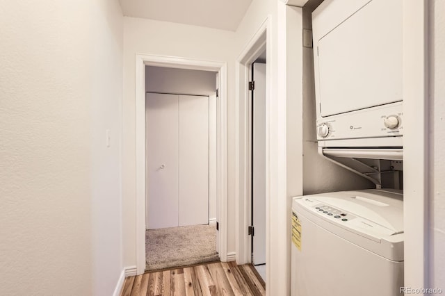 laundry room featuring laundry area, light wood-style flooring, stacked washer and dryer, and baseboards