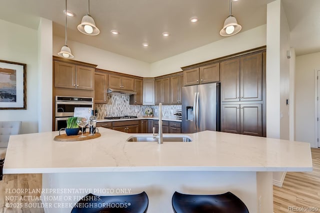 935 W 128th Pl, Westminster, CO 80234 - kitchen featuring appliances with stainless steel finishes, under cabinet range hood, light wood-type flooring, hanging light fixtures, and backsplash