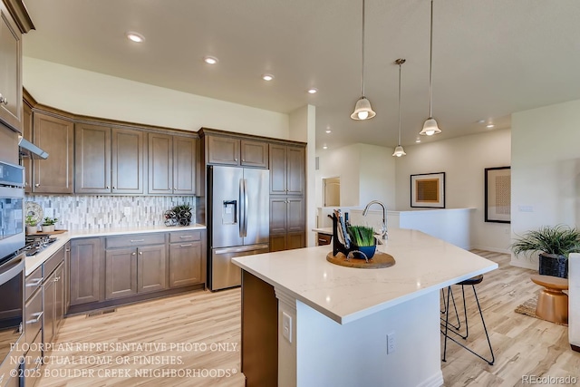 935 W 128th Pl, Westminster, CO 80234 - kitchen featuring appliances with stainless steel finishes, light wood-style flooring, tasteful backsplash, a center island with sink, and a breakfast bar area