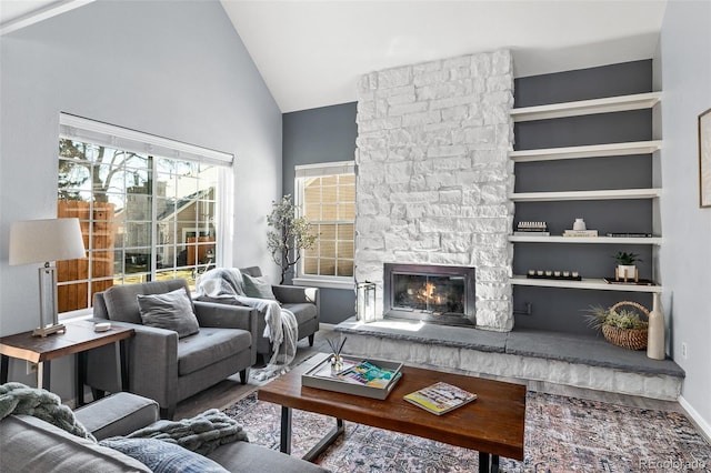 living area with baseboards, built in features, wood finished floors, a fireplace, and high vaulted ceiling