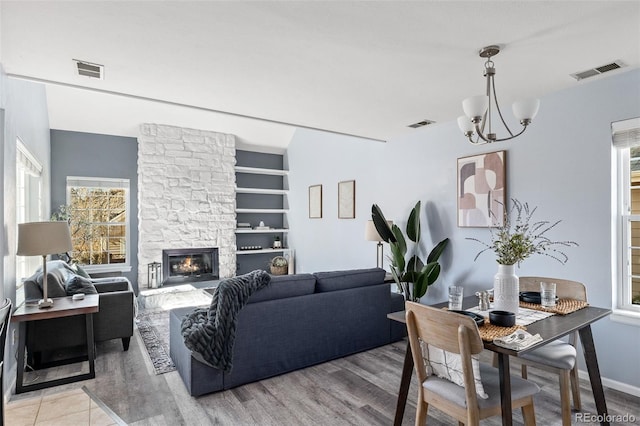 living room featuring light wood-style floors, a fireplace, visible vents, and built in shelves