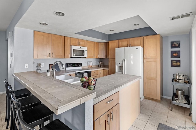 kitchen featuring a peninsula, white appliances, a sink, visible vents, and tile counters