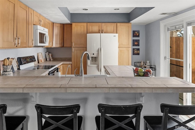 kitchen with a peninsula, white appliances, tile counters, and a kitchen breakfast bar