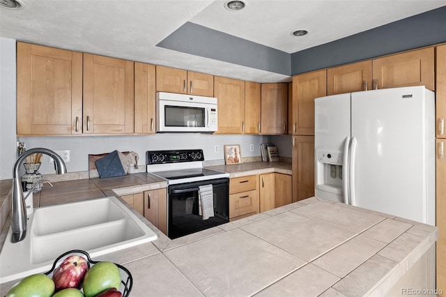 kitchen featuring a peninsula, white appliances, tile counters, and a sink